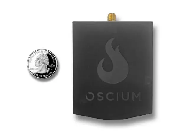 An Oscium Wi-Pry 2500x device for spectrum analysis, shown next to a quarter for scale, featuring a black casing with the Oscium logo.