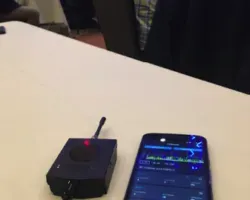 Smartphone next to a WiPry 2500x device with an antenna, showing a spectrum‑style graph used for dual‑band Wi‑Fi analysis.